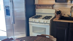 Cozinha com armários de madeira, geladeira de aço inoxidável, fogão branco e mesa de jantar com jogos americanos.