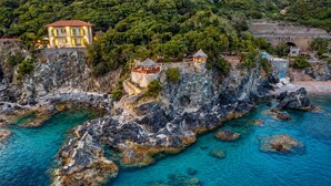 A coastal property with a stone staircase leading to a building, clear turquoise waters, and lush greenery.