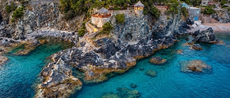 A coastal property with a stone staircase leading to a building, clear turquoise waters, and lush greenery.