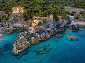 A coastal property with a stone staircase leading to a building, clear turquoise waters, and lush greenery.