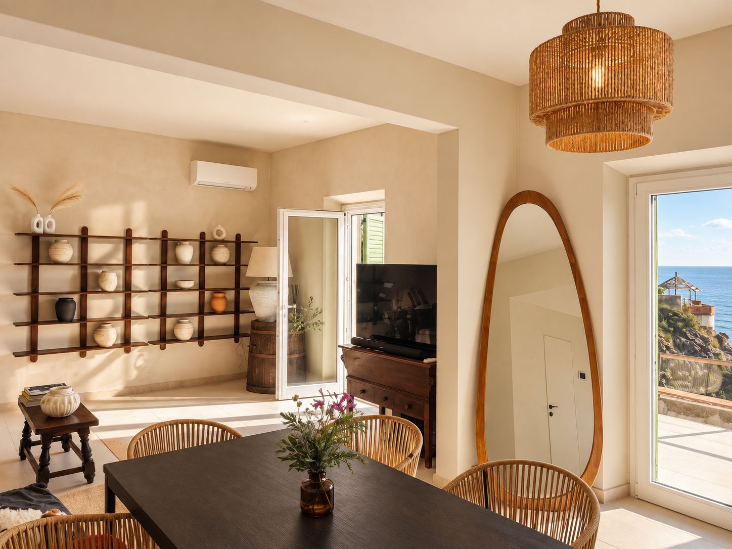 A dining area with a dark wooden table, wicker chairs, a large mirror, and a wall-mounted shelf with decorative items.