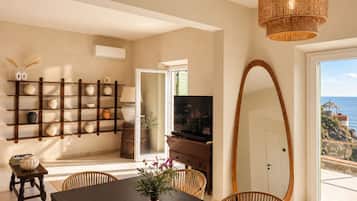 A dining area with a dark wooden table, wicker chairs, a large mirror, and a wall-mounted shelf with decorative items.
