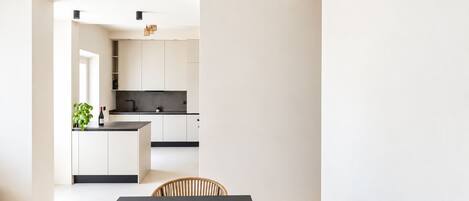 A modern kitchen with white cabinets, a black countertop, and a hanging light fixture.