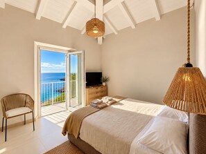 Une chambre à coucher avec un lit, une télévision, une chaise et un balcon donnant sur la mer.