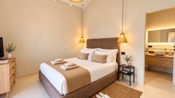 A modern bedroom with a large bed, bedside lamps, a TV, and a bathroom visible through an open door.