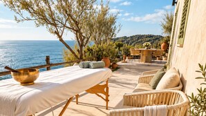 A terrace with a table, chairs, a record player, and a view of the sea.