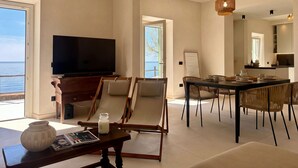 A modern living room with a TV, seating, a dining area, and a view of the sea. - Roc Villa - 2 Private Beach Accesses  (Rosignano Marittimo)