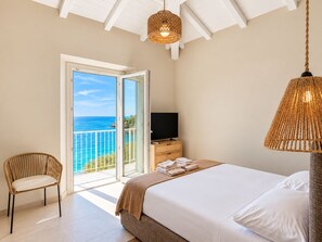A bedroom with a bed, a television, a chair, and a view of the sea through a glass door. - Roc Villa - 2 Private Beach Accesses  (Rosignano Marittimo)