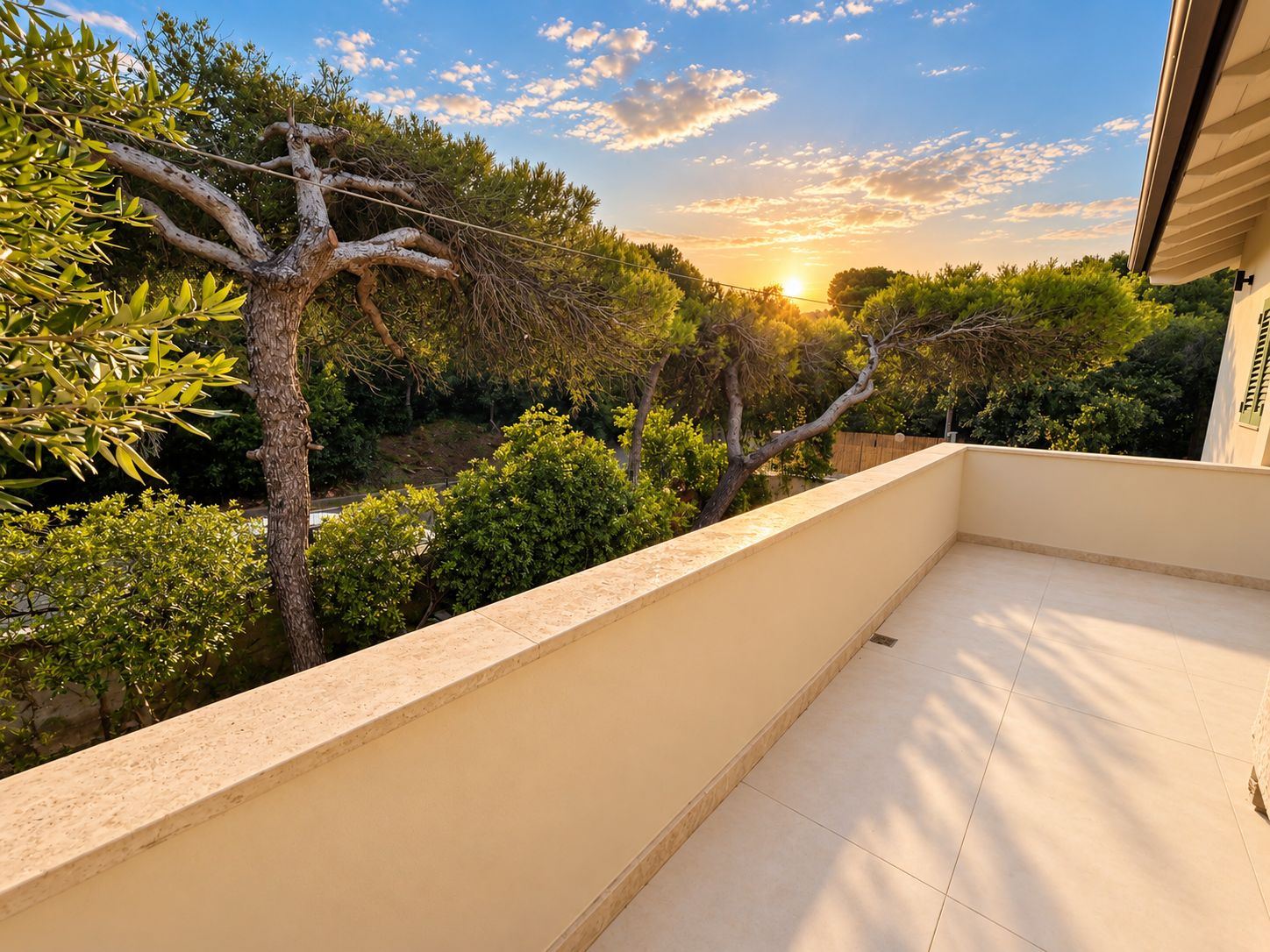 A balcony with a view of a garden and trees, a tiled floor, and a clear sky.