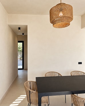 A modern dining area with a dark table and woven chairs, a woven pendant light, and a view through an open doorway. - Roc Villa - 2 Private Beach Accesses  (Rosignano Marittimo)