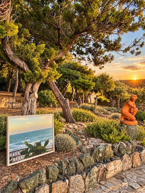 A garden with a statue, a framed picture, and a rocky border. - Roc Villa - 2 Private Beach Accesses  (Rosignano Marittimo)