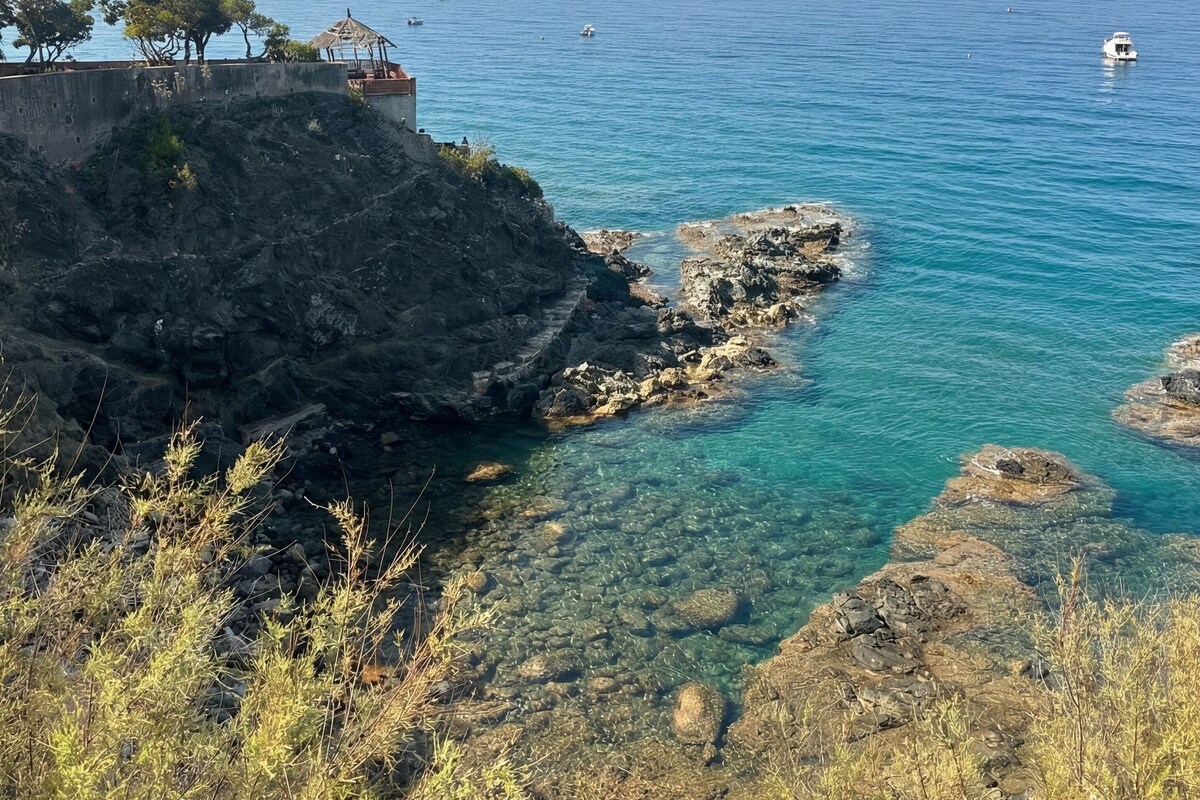 Paisaje costero con aguas azul turquesa, terreno rocoso y vegetación escasa.