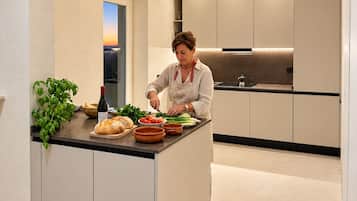 Una cocina moderna con una isla central, una persona preparando comida y vista al atardecer a través de una ventana.