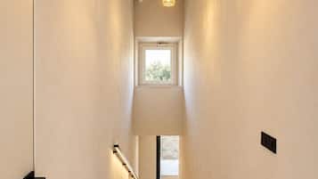 A narrow hallway with a staircase leading to a second floor, a window at the top, and a hanging light fixture.
