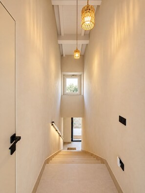 A narrow hallway with a staircase leading to a second floor, a window at the top, and a hanging light fixture. - Roc Villa - 2 Private Beach Accesses (Rosignano Marittimo)