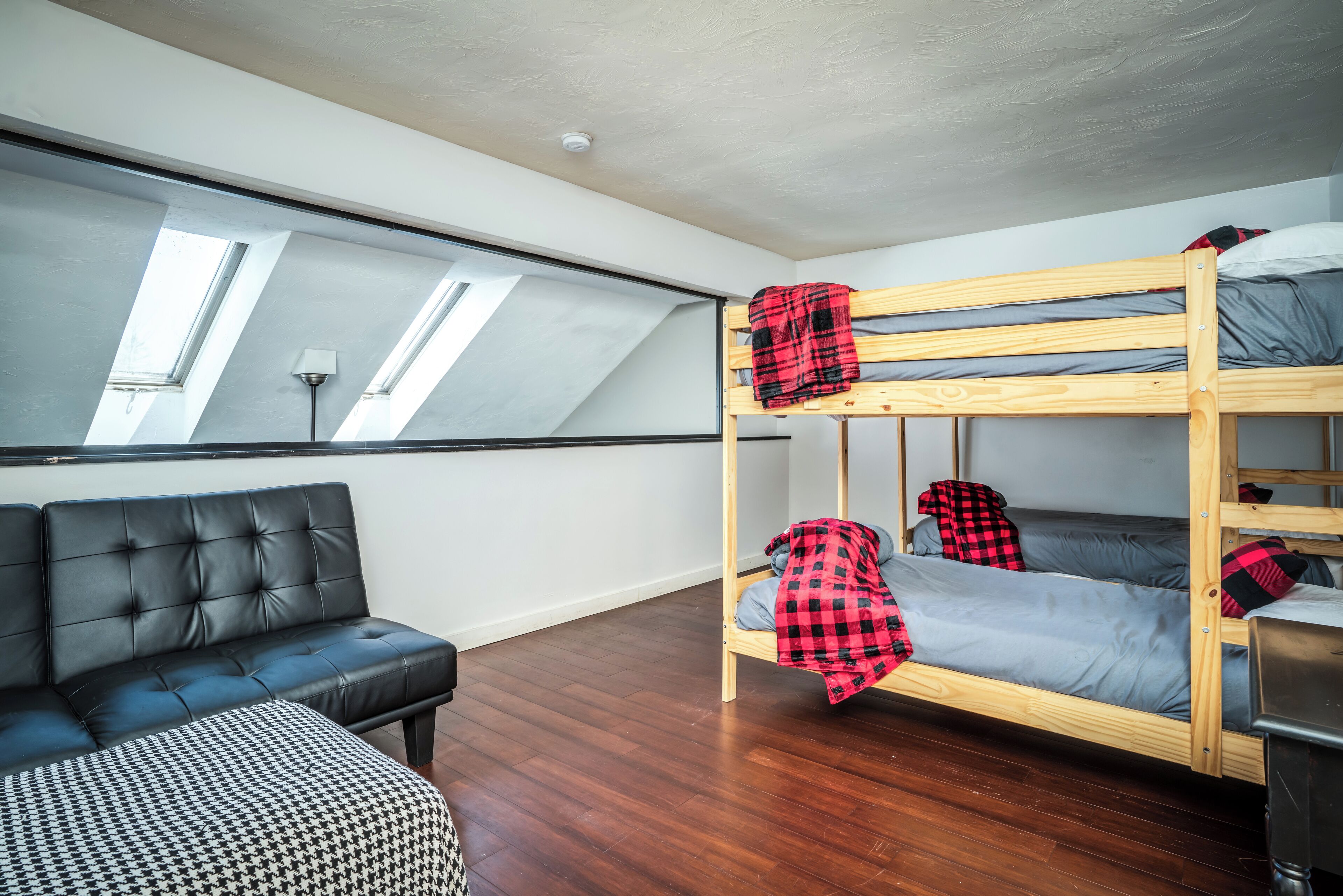 A room with a bunk bed, a leather sofa, and a patterned ottoman.