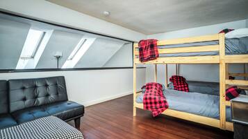 A room with a bunk bed, a leather sofa, and a patterned ottoman.