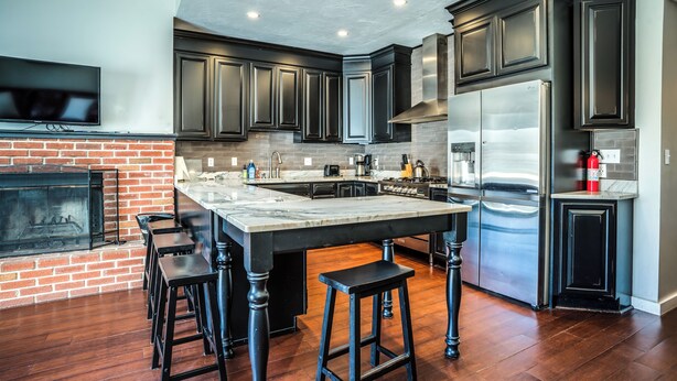 A modern kitchen with dark cabinetry, a large island, and a built-in fireplace. - Tenney Mountain Retreat, Plymouth & Rumney, NH (Plymouth)