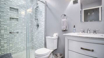 A modern bathroom with a glass shower enclosure, a white toilet, a sink with a mirror, and a trash can.