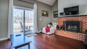 A living room with a fireplace, a television mounted above it, and a sliding glass door leading to an outdoor area. - Tenney Mountain Retreat, Plymouth & Rumney, NH (Plymouth)