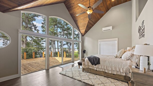 A bedroom with a large window, a ceiling fan, and a bed with a white comforter.
