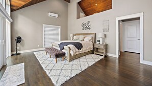 A bedroom with a bed, bedside tables, a ceiling fan, a large window, and a door.
