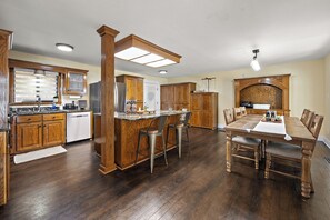 Eine geräumige Küche mit Holzausbau, einer zentralen Kochinsel mit Barhocker und einem Esstisch mit Stühlen.
