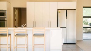 Eine moderne Küche mit weißen Schränken, einer eingebauten Mikrowelle und einem Kühlschrank. Es gibt drei hölzerne Barhocker mit gepolsterten Sitzen.