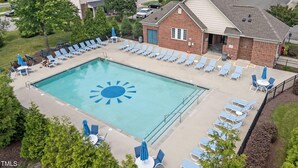 A swimming pool with sun-shaped tiles, surrounded by lounge chairs and umbrellas, set in a residential area with houses in the background. - Entire home in prime Raleigh with workspace, comm pool, dog park and golf course (Raleigh)