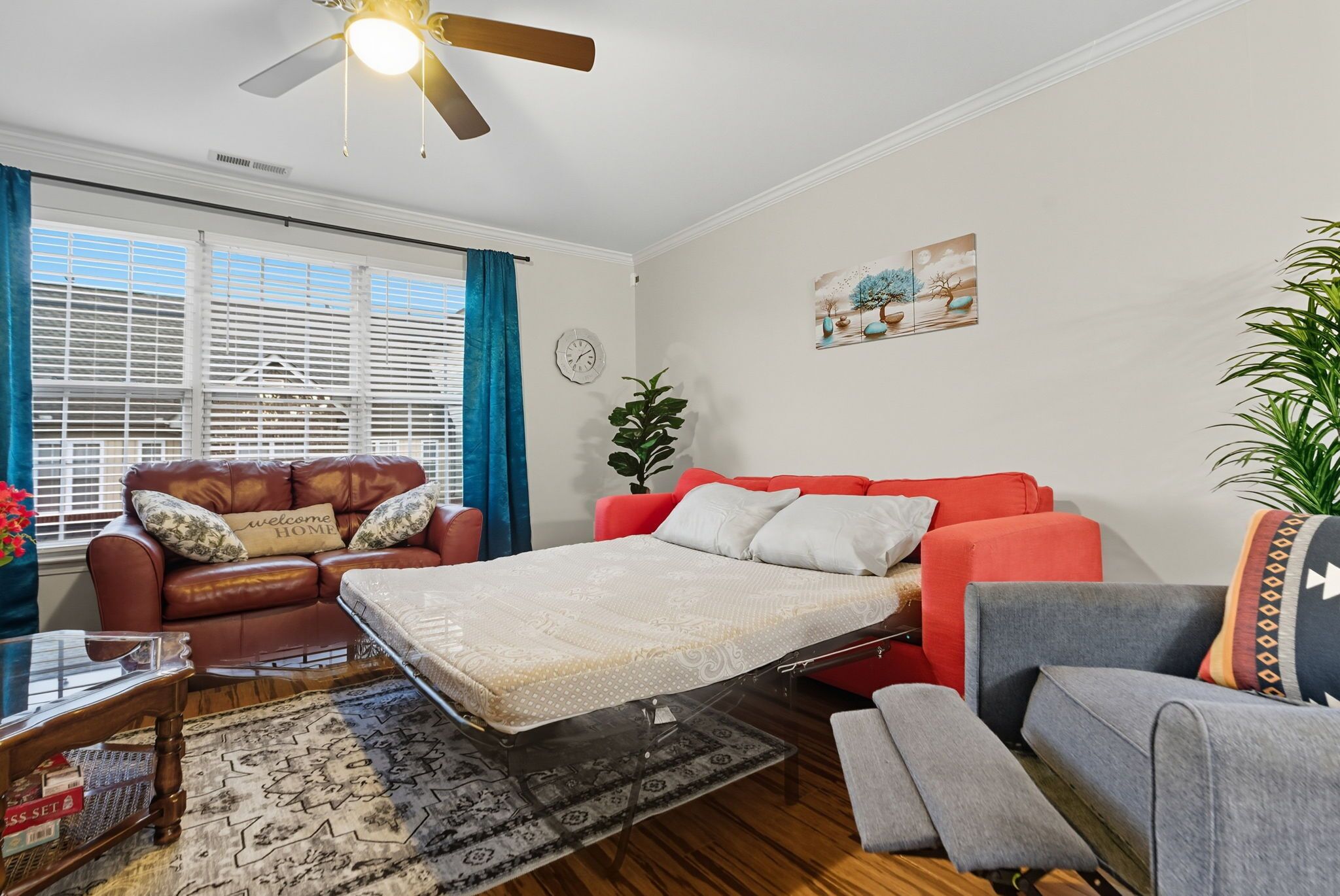 A living room with a sofa, a red couch, a grey armchair, a coffee table, and a ceiling fan.