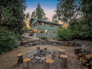 Una casa de dos pisos con un patio, rodeada de árboles y una chimenea.