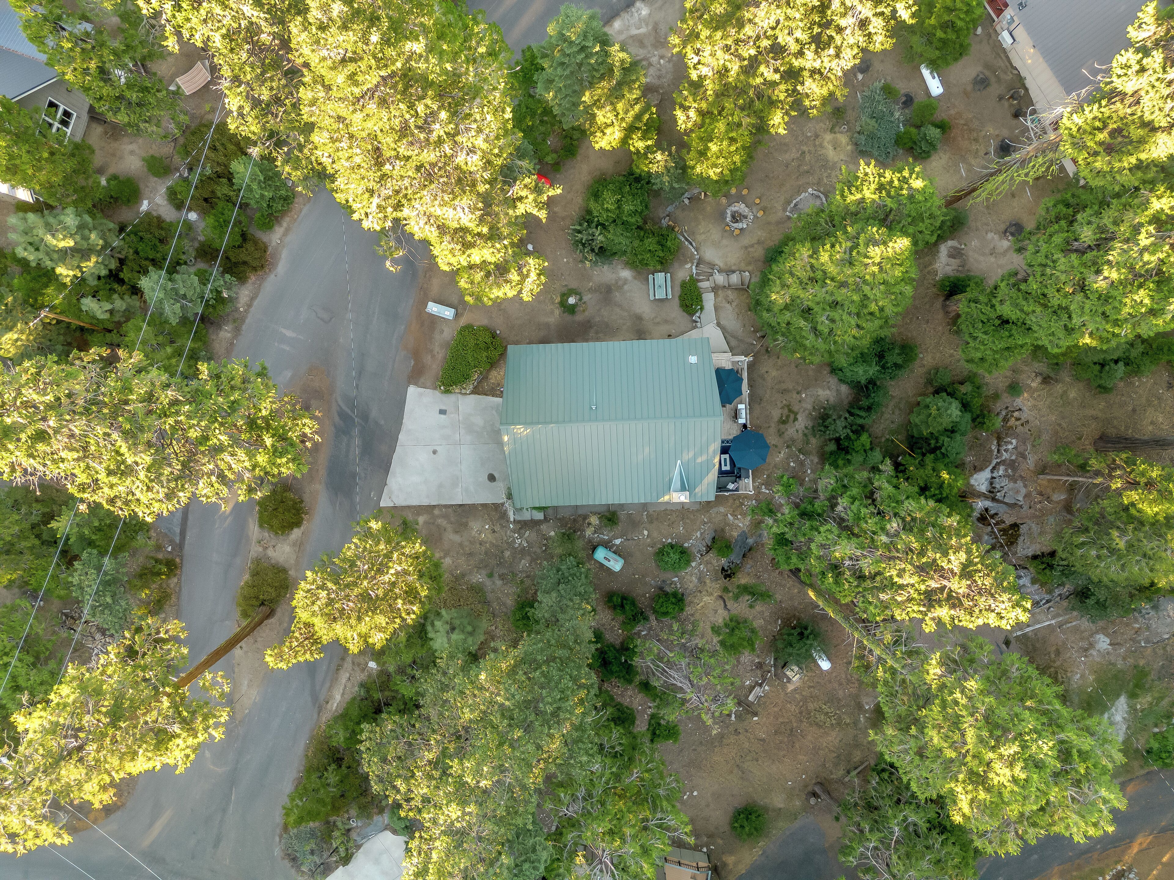 An aerial view of a residential property with a green-roofed house, a paved driveway, and surrounding greenery.