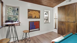 A room with a pool table, a wooden ceiling, and a window with a view of trees.