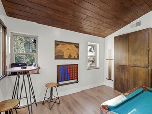 Una habitación con mesa de billar, techo de madera y ventana con vistas a árboles.