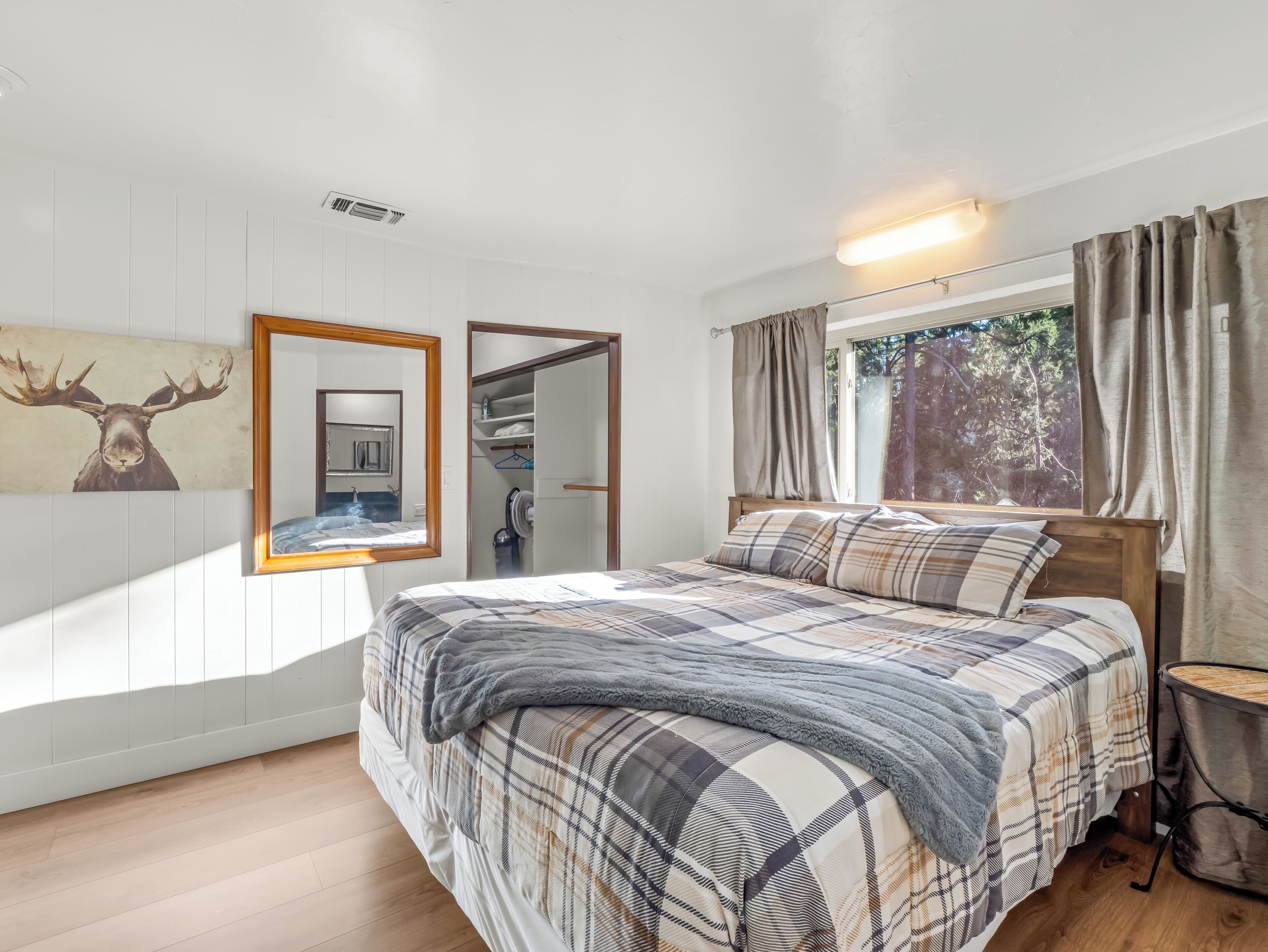 A bedroom with a bed, a mirror, a wardrobe, a window with curtains, and a wall-mounted light fixture.