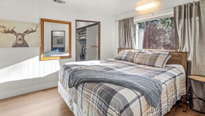 A bedroom with a bed, a mirror, a wardrobe, a window with curtains, and a wall-mounted light fixture.