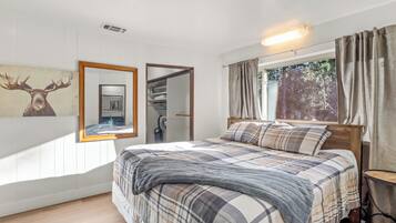 A bedroom with a bed, a mirror, a wardrobe, a window with curtains, and a wall-mounted light fixture.