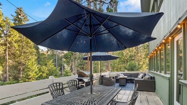 An outdoor patio with a table and chairs, a grill, and a large umbrella providing shade.