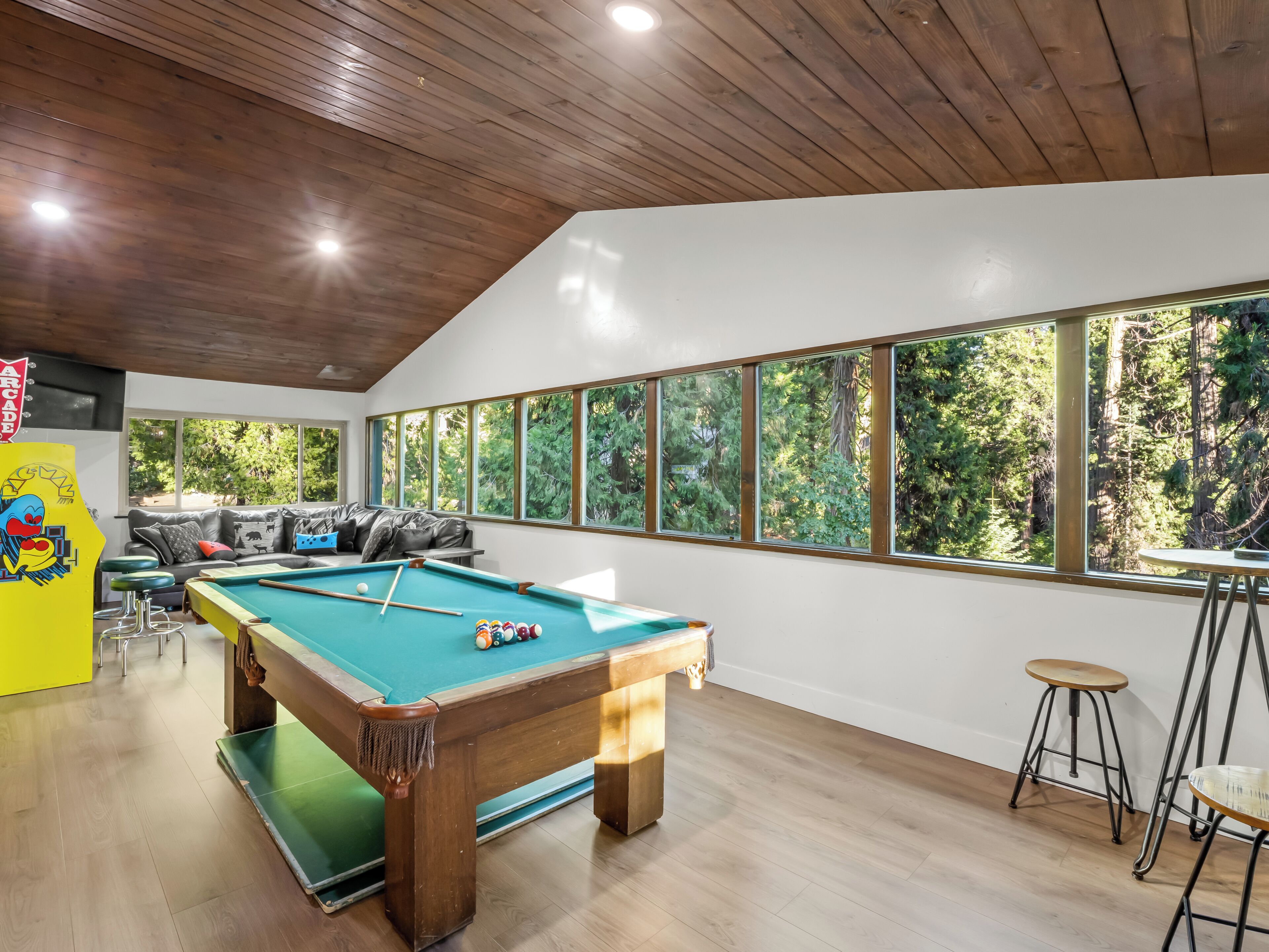 A pool table with a green felt surface, a sofa with cushions, and a bar area with stools.