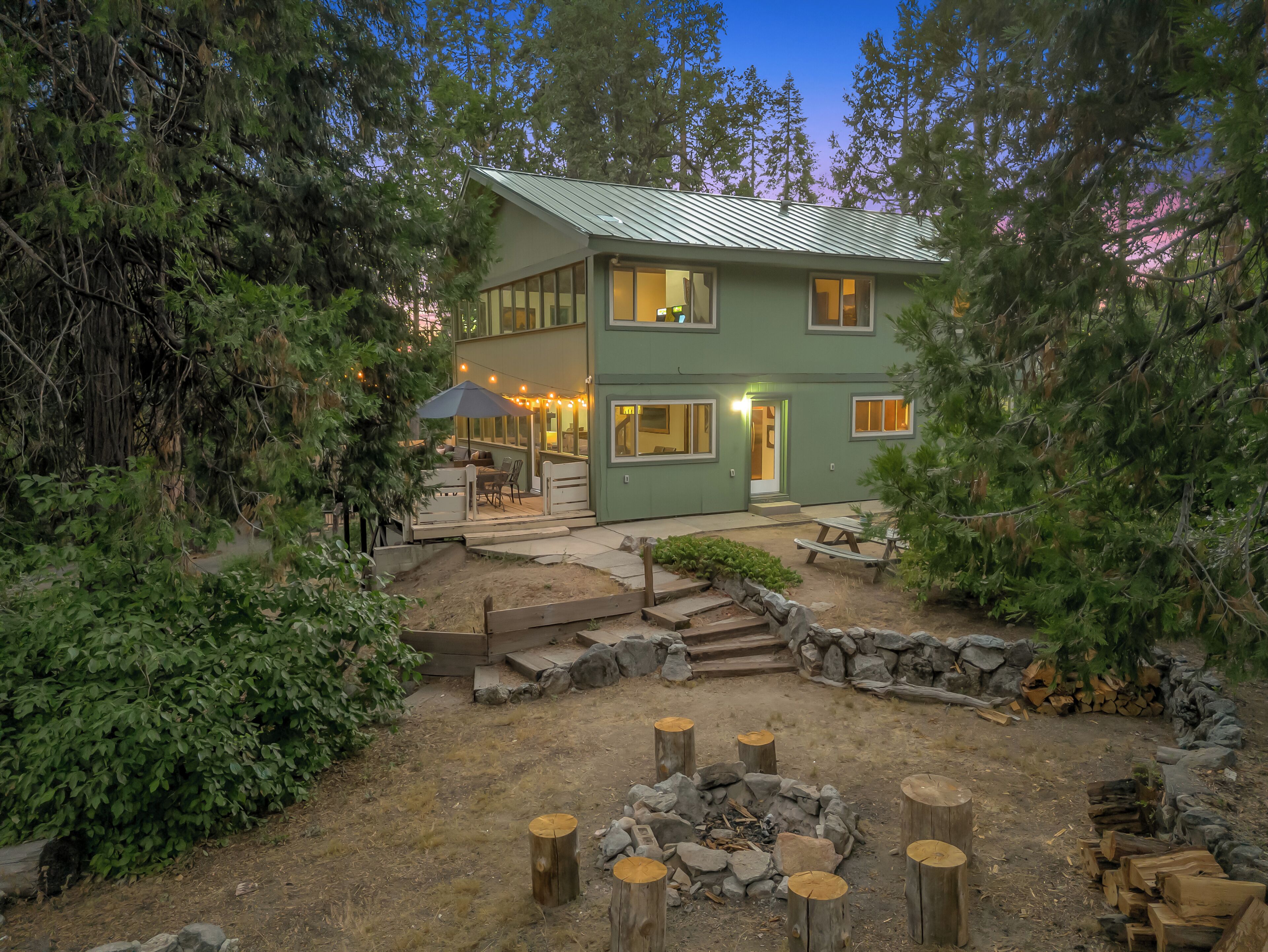 A two-story house with a patio area, a stone fire pit, and a covered seating area.