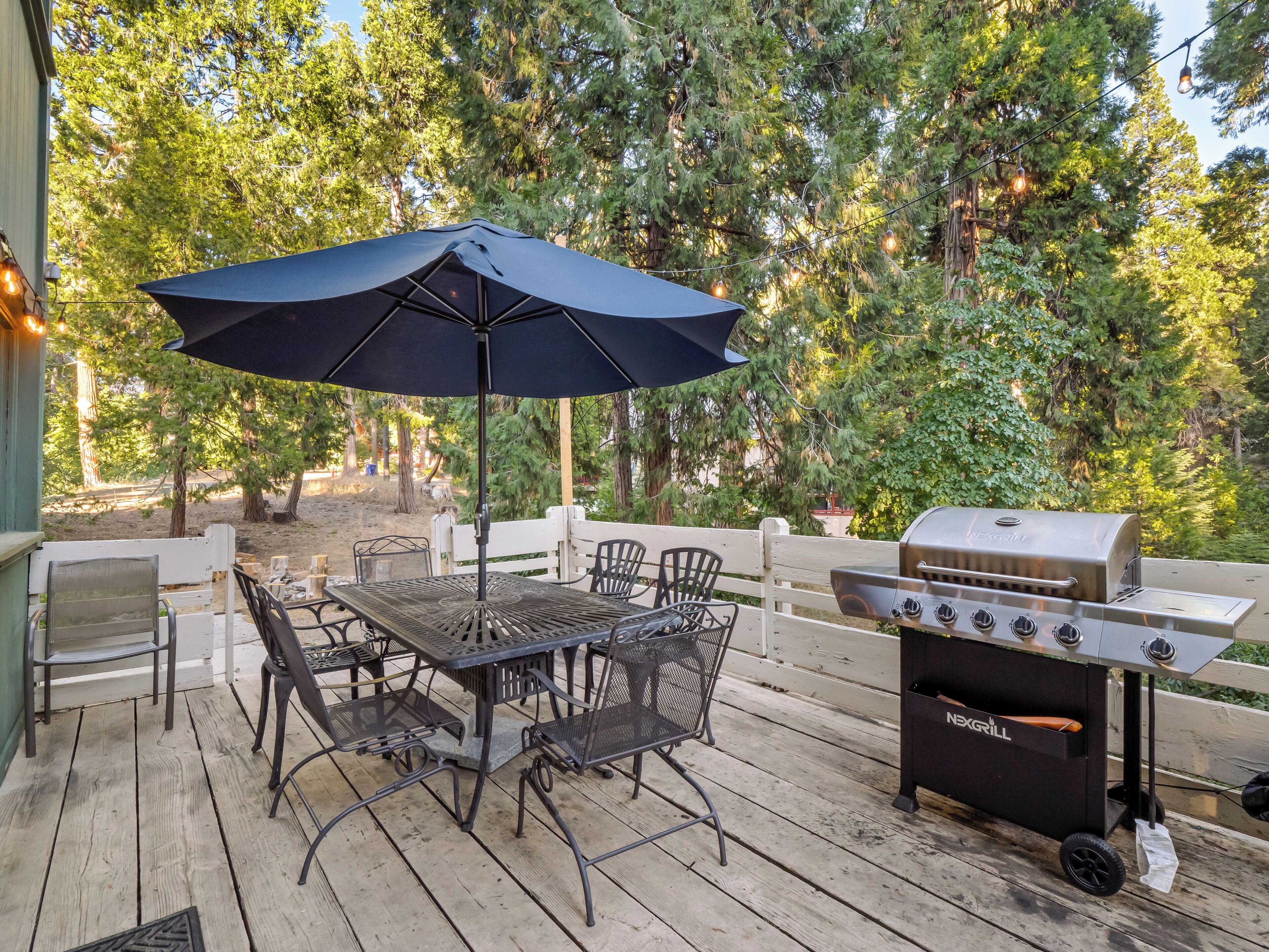 An outdoor patio with a table and chairs, a barbecue grill, and an umbrella.