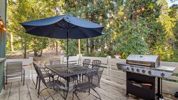 An outdoor patio with a table and chairs, a barbecue grill, and an umbrella.