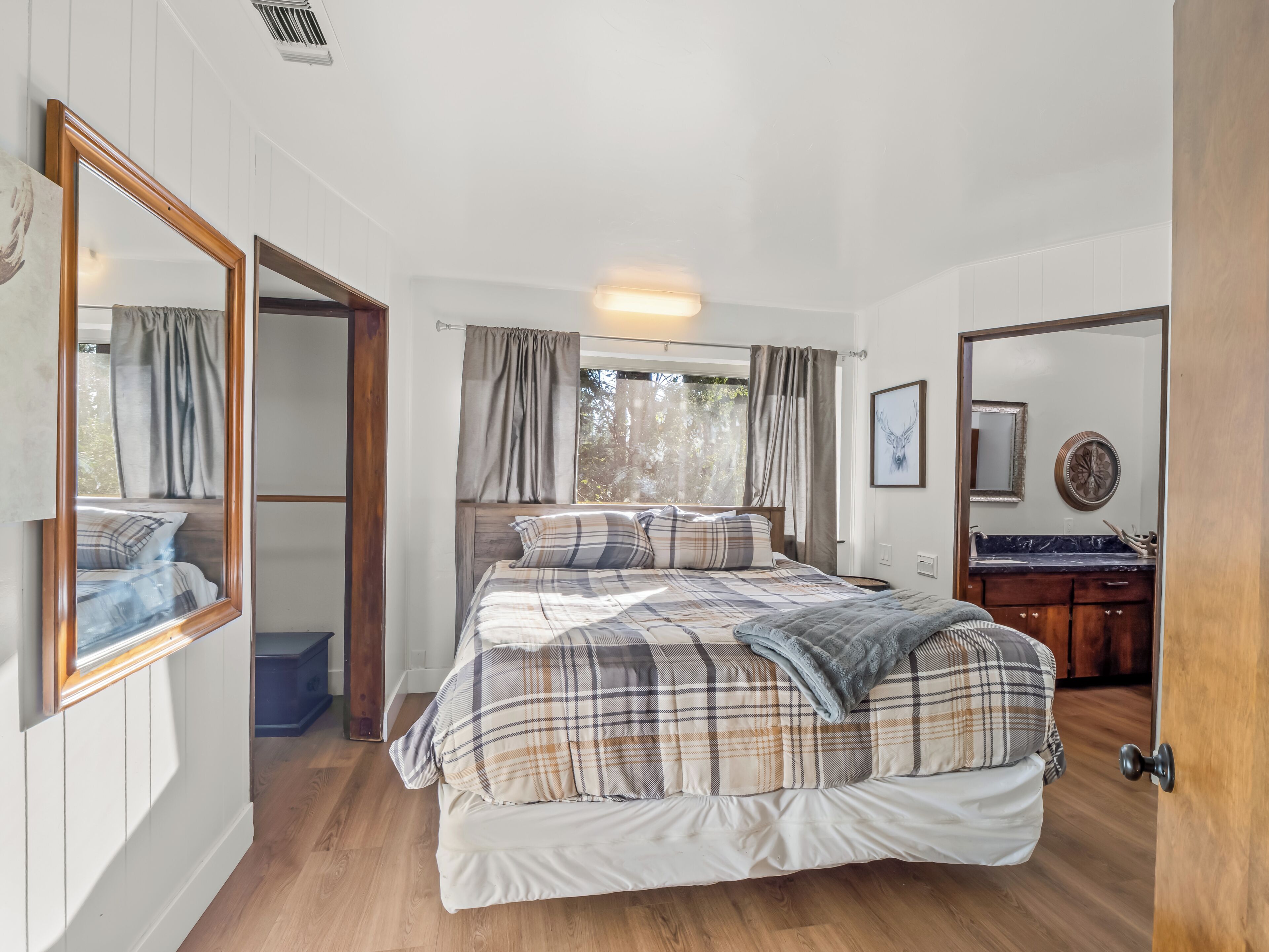 A bedroom with a bed, a mirror, a window with curtains, and a wooden floor.