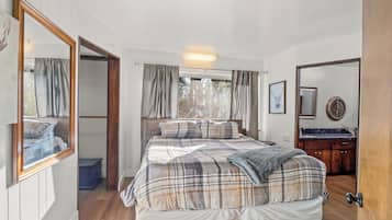 A bedroom with a bed, a mirror, a window with curtains, and a wooden floor.