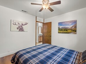 Un dormitorio con cama, ventilador de techo, una puerta y dos cuadros colgados en la pared.
