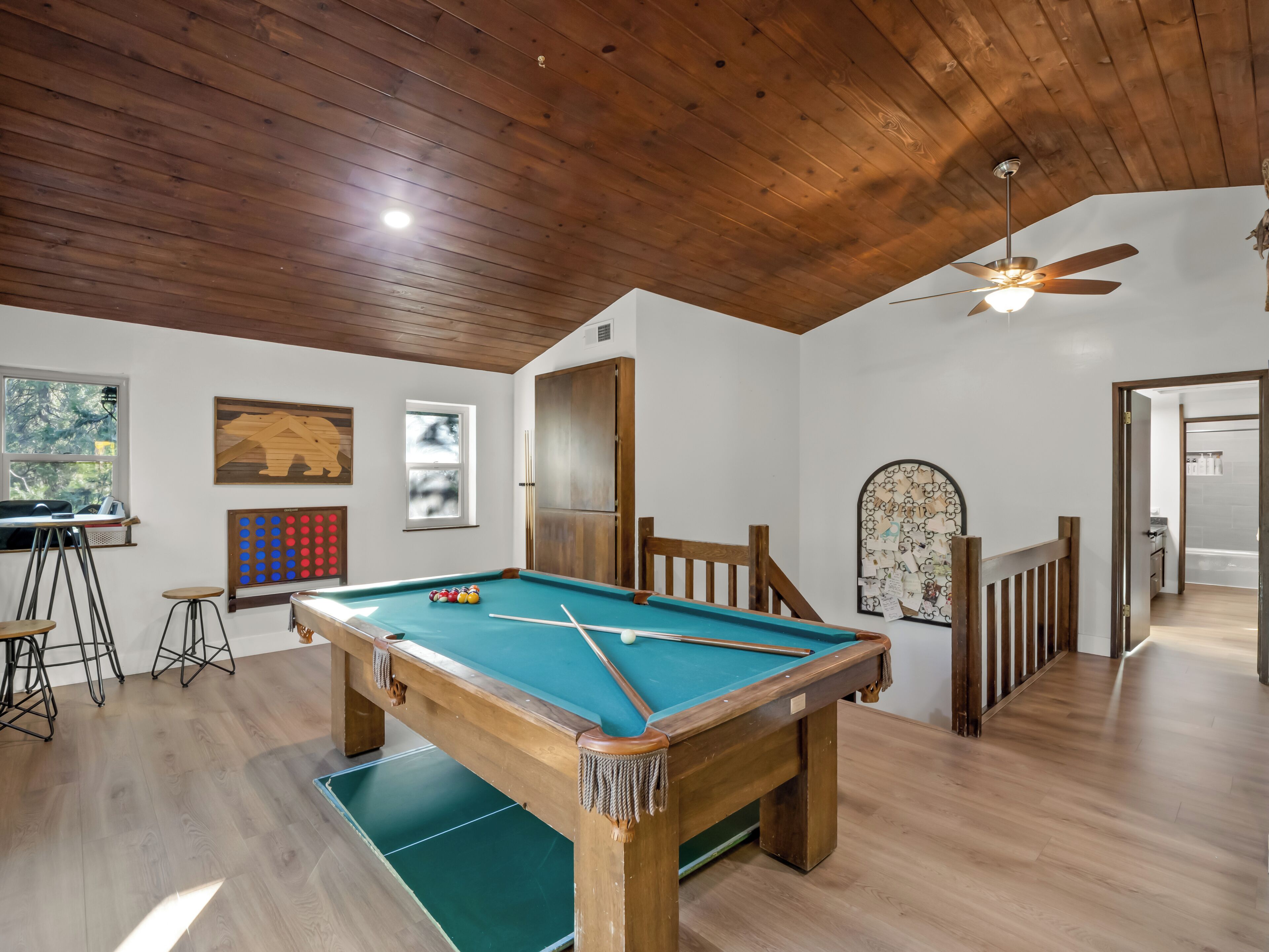 A pool table in a room with wooden flooring and a ceiling fan.