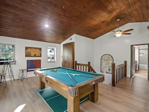 A pool table in a room with wooden flooring and a ceiling fan.