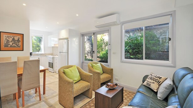 A modern living room with a sofa, two armchairs, a dining table, and a kitchen area. - Cedar Rest Studio (Katoomba)