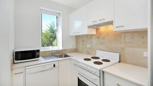 A compact kitchen with white cabinets, a microwave, a sink, and a stove. - Cedar Rest Studio (Katoomba)
