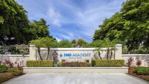A sign for IMG Academy in Bradenton, Florida, with a statue, greenery, and a clear sky.